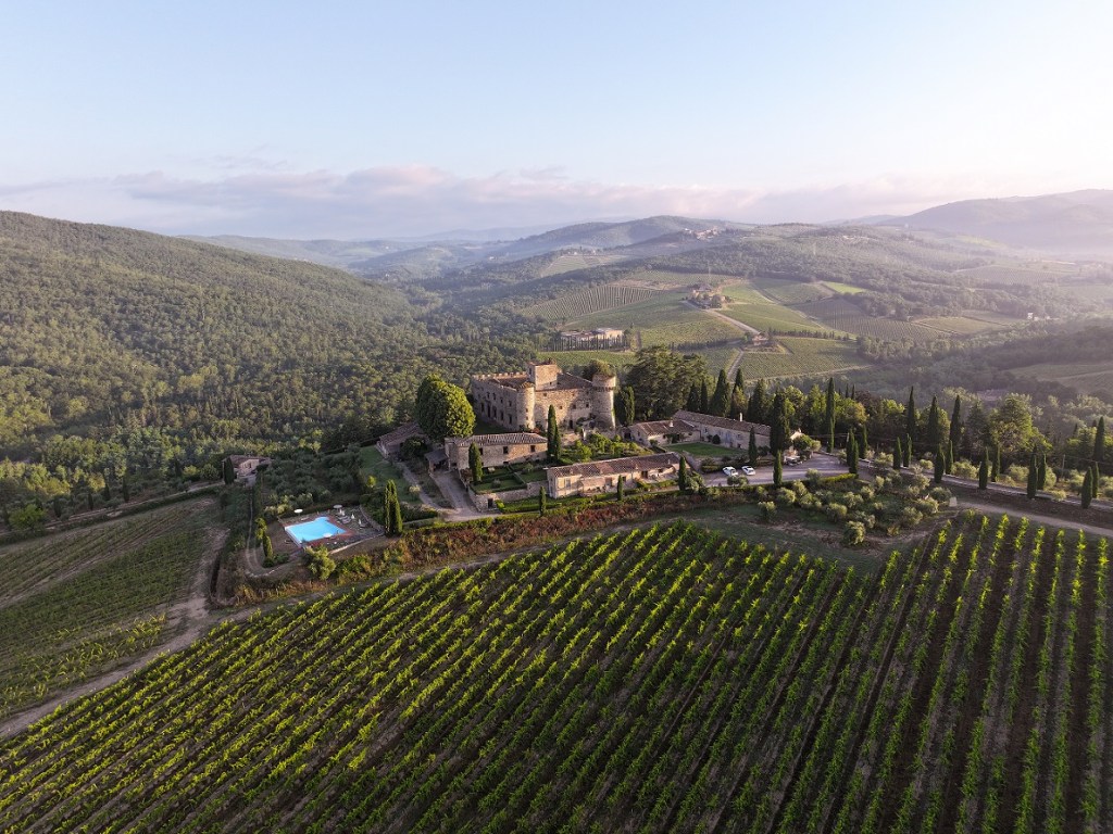 Vista aerea di un castello circondato da vigneti e colline in Toscana, Italia, con una piscina visibile.